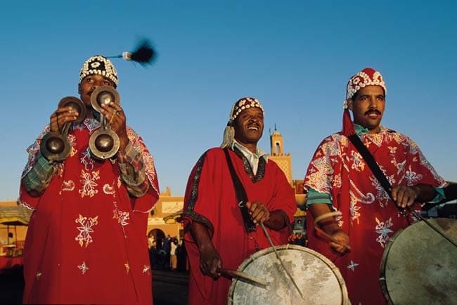 Gnaoua musicians in red embroidered robes playing qraqeb metal castanets and drums in Essaouira, Morocco