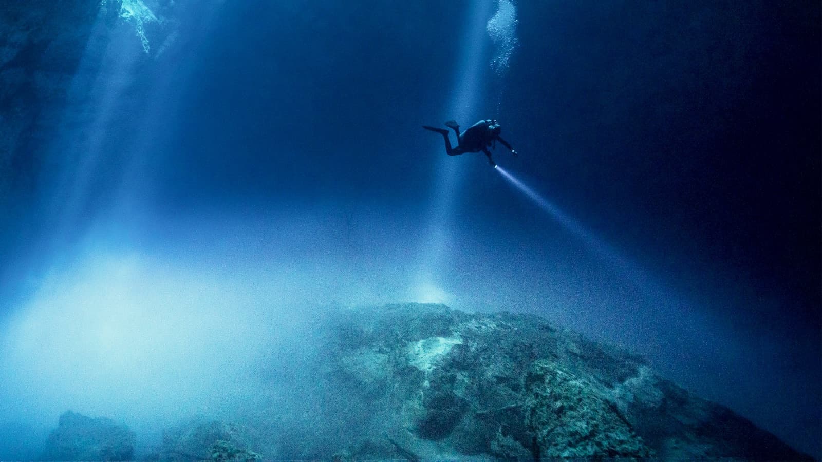Scuba diver suspended in shafts of light entering a Yucatán cenote in Mexico