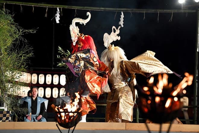 Noh actors in silk robes and wooden masks performing Takigi Noh by bonfire at Heian Shrine in Kyoto