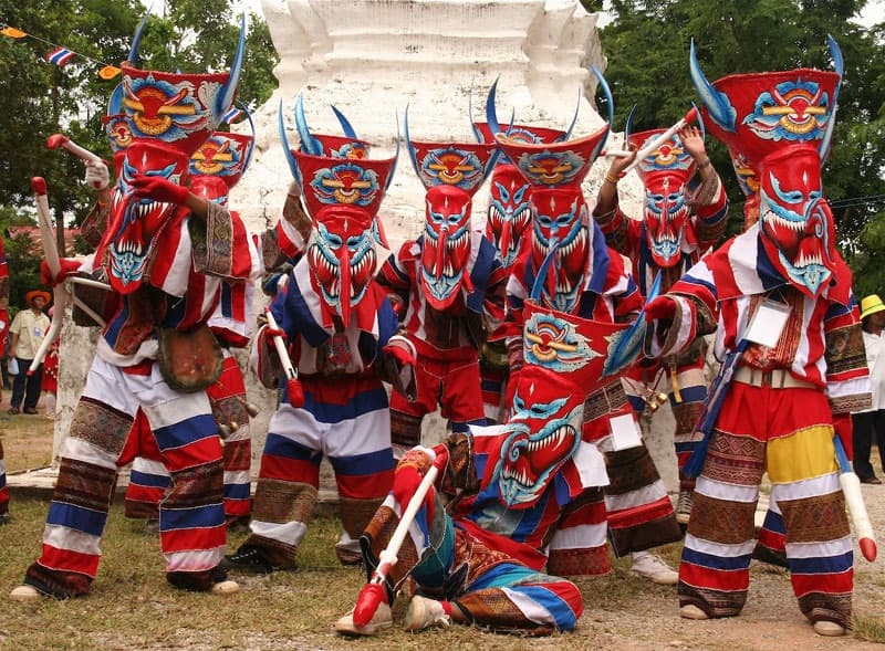 Performers in hand-carved Phi Ta Khon ghost masks with red, white, and blue patchwork costumes in Dan Sai, Thailand