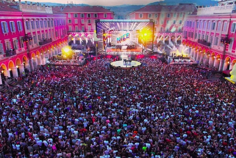 Massive crowd in front of a colorfully lit stage at a Fête de la Musique celebration in France