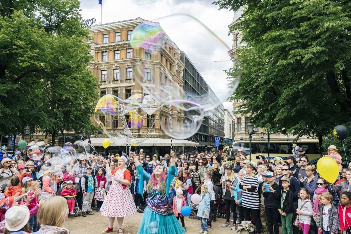 Giant soap bubbles drifting through a crowd at Helsinki Day celebrations in front of historic city architecture