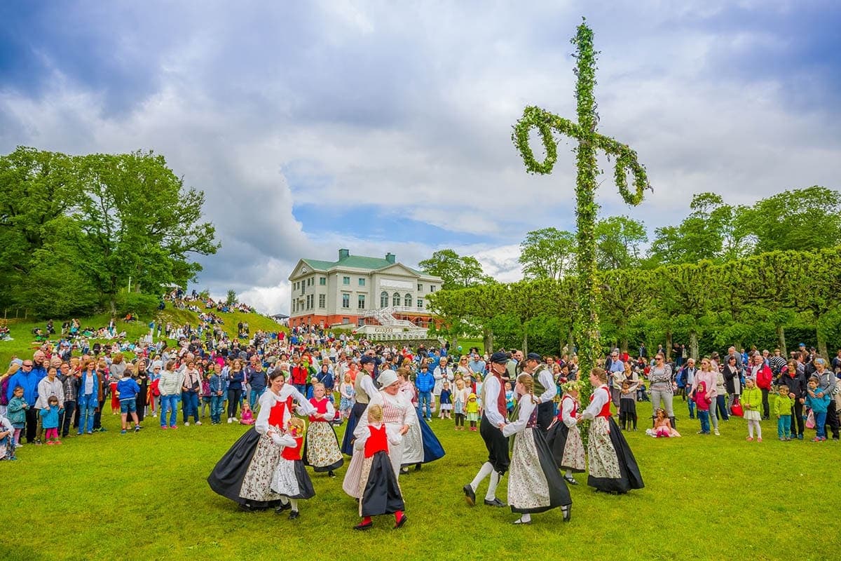 Swedish midsummer maypole decorated with birch leaves and wildflowers, surrounded by dancers in folk dress